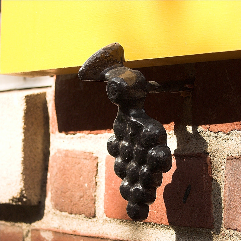 Closeup of Lag Mount Vintage Grape Shutter Tieback with black powder coating installed on yellow shutter.